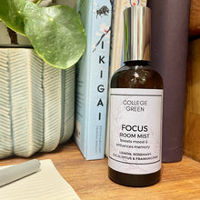 Amber glass bottle of College Green Focus Room Mist sitting on a desk with potted plant and books