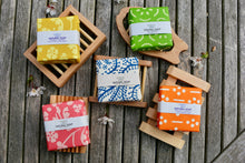Five wrapped soaps, each sat on a wooden soap dish