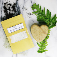 Wax paper sachet of Warming foot soak and heart shaped bar of Peppermint + Rosemary soap. Coffee grounds and green fern leaves