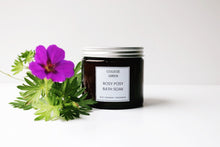 Amber glass jar of Rosy Posy bath soak on a white background with purple geranium flower
