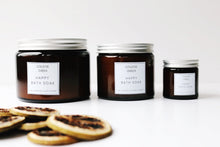 Three amber glass jars of Happy Bath Soak, large, medium and small. Slices of lime in the foreground